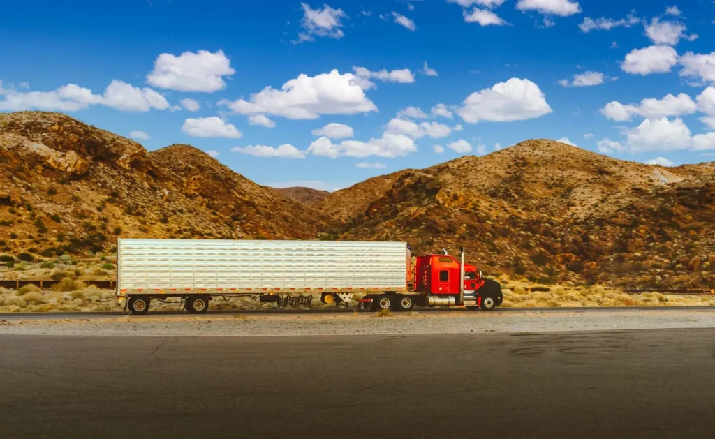 Red semi-truck and enclosed trailer on a highway through dry hills