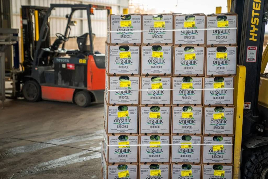 Pallet of boxed organic broccoli beside a forklift in a warehouse