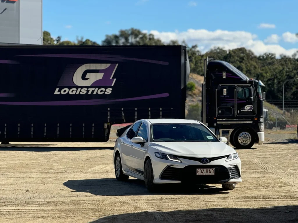 White sedan parked beside a freight truck at a loading area