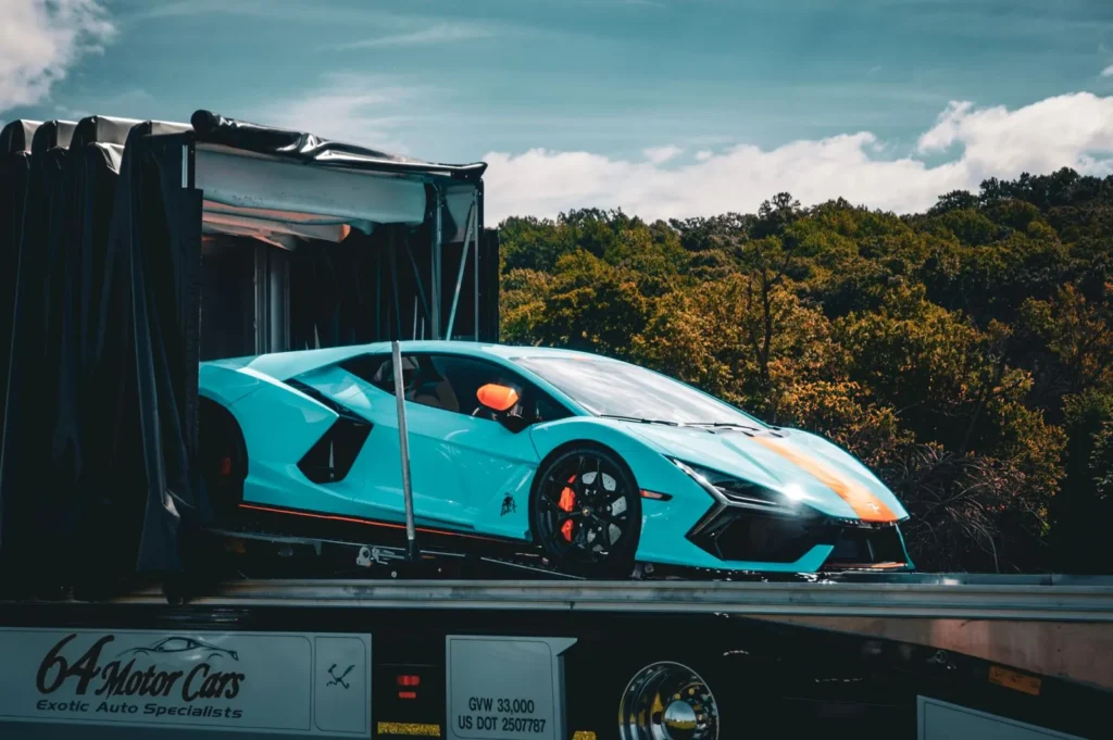 Blue sports car on a transport platform beside a covered trailer