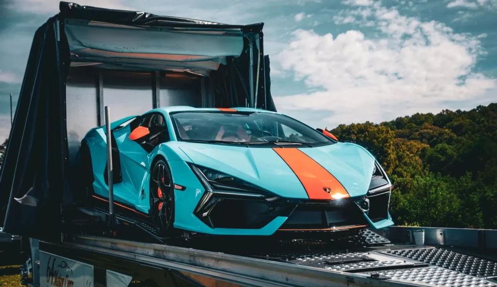 Blue sports car being unloaded from a covered vehicle transport trailer