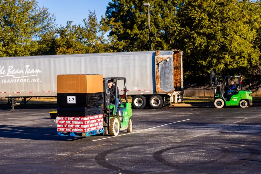 Forklift carrying a wrapped pallet near an open freight trailer
