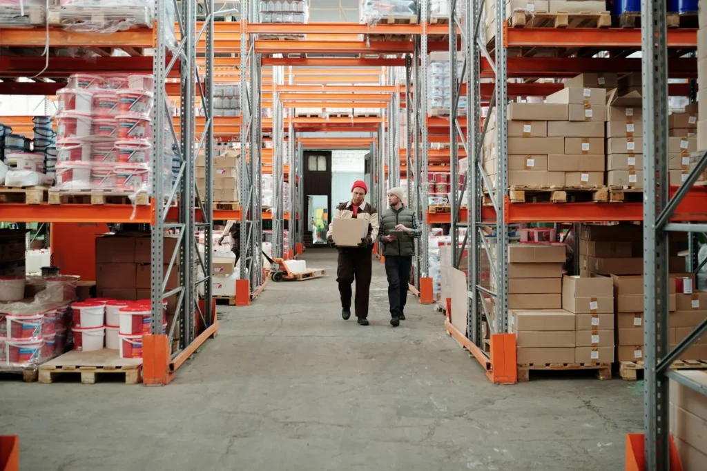 Two warehouse workers reviewing a carton between storage racks