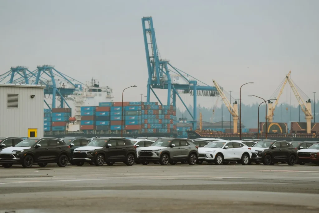 Rows of new cars staged beside cranes and containers at a seaport