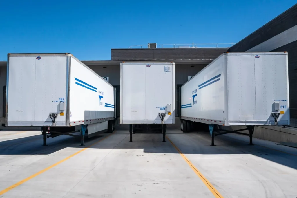Three enclosed freight trailers parked at warehouse docks