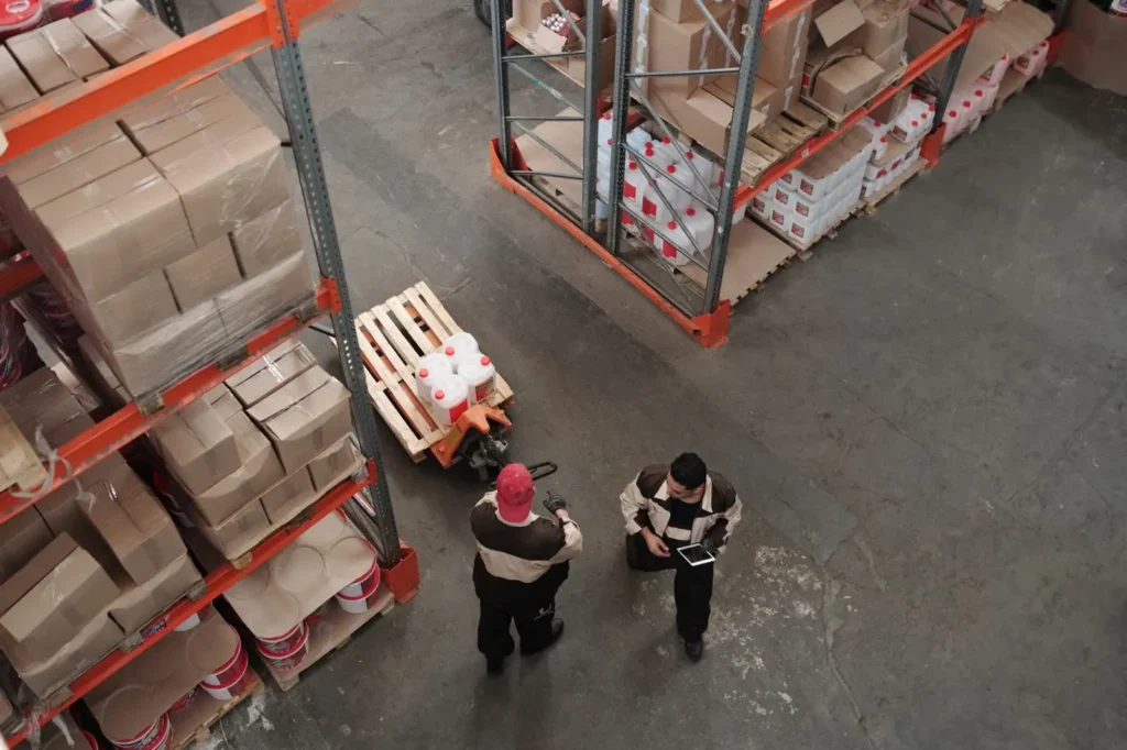 Two warehouse workers checking stock beside racks of cartons